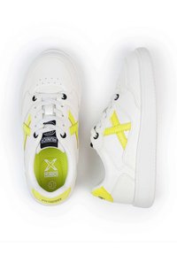 Zapatillas sintéticas blancas con punta redonda, acentos amarillos, ojales negros y una plantilla de malla texturizada. Diseño clásico con cordones.