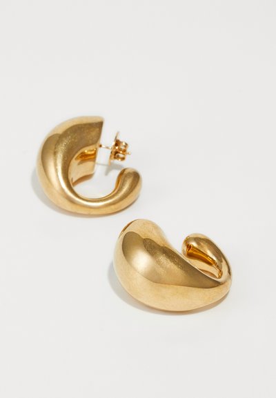 Boucles d'oreilles en métal doré au design lisse et sculptural. Forme courbée avec une finition brillante et une fermeture à clou.