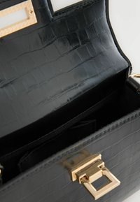 Sac à main en cuir noir avec une texture crocodile, doté d'un fermoir en métal doré et d'un intérieur spacieux doublé de tissu noir.