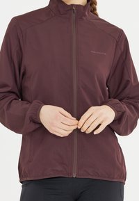 Bordeaux lehká bunda s vysokým límcem, zipem vpředu, elastickými manžetami a decentním logem na hrudi. Hladká textura a přiléhavý střih.