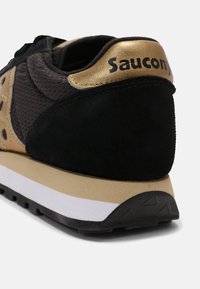Sorte og gull sneakers laget av mesh- og semsket skinnmaterialer. Har en tykk hvit mellomsåle og en svart gummisåle. Merkenavnet "Saucony" er på hælen.
