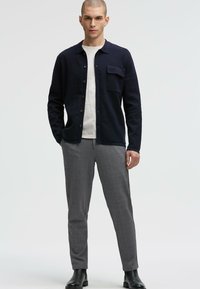 Marineblaues Hemd mit Knöpfen und Brusttasche, kombiniert mit grauen karrierten Hosen und schwarzen Ankle-Boots. Glattes Gewebe und taillierte Passform.