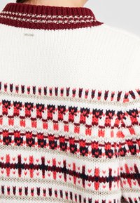 Sweter dzianinowy z białą bazą i bordowym ściągaczem. Posiada geometryczny wzór w kolorze czerwonym i granatowym, podkreślony złotą nitką.