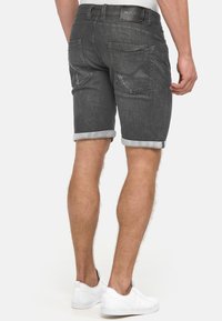 Shorts en denim gris avec un revers roulé, cinq poches et un patch de ceinture en cuir. Texture lisse et détails d'usure minimes.