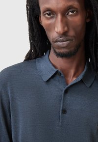 Mørkeblå polo-shirt med et struktureret stof, en klassisk krave og tre foran knapper, der viser et tætsiddende design.
