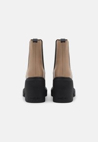 Bottines marron et noires avec un dessus en cuir lisse, une semelle plateforme épaisse et des tirants à l'arrière pour un enfilage facile.