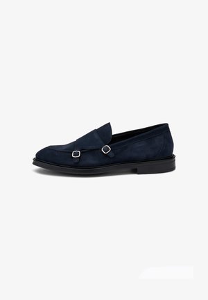 Mocasines de ante azul marino con punta redonda, que presentan dos hebillas decorativas y una suela plana de goma negra. Textura suave y detalles cosidos.