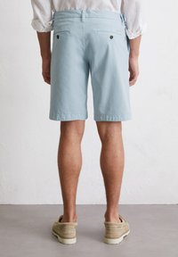Shorts bleu clair à coupe droite, fabriqués en tissu doux. Dotés de poches arrière avec des boutons noirs et d'une taille élastique.