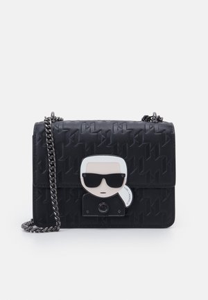 Black crossbody bag with embossed pattern, silver chain strap, and a clasp featuring a stylized face wearing dark sunglasses.