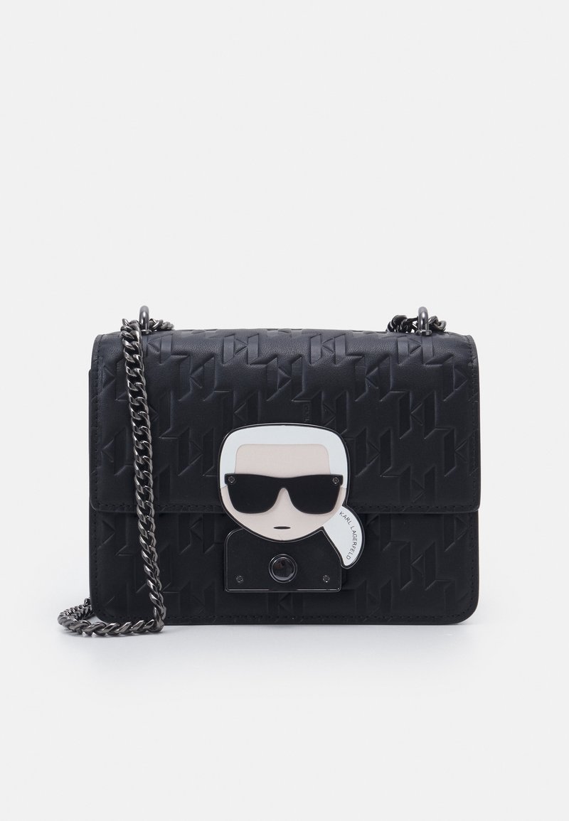 Black crossbody bag with embossed pattern, silver chain strap, and a clasp featuring a stylized face wearing dark sunglasses.