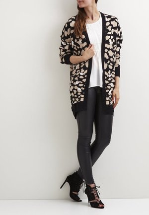 Cardigan en imprimé léopard noir et beige, à l'avant ouvert, à manches longues, associé à des leggings en simili cuir noirs et des talons à lacets noirs.