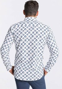 Weißes langärmliges Hemd mit blauem kreisförmigen Muster, mit Kragen und knöpfbaren Ärmeln. Weicher Stoff, taillierte Passform.