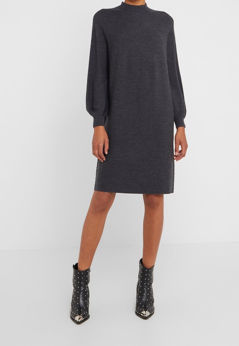 Robe grise en tricot avec de longues manches ballon, un col montant et une coupe droite, associée à des bottines noires ornées de clous.