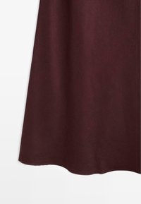 Kant på en mørkerød A-formet nederdel med subtil struktur, vist mod en hvid baggrund.