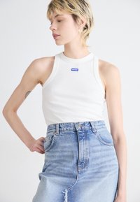 Vit ribbad linne med hög hals och en liten blå "HUGO" etikett, matchad med högmidjade ljusblå denimshorts med fransad fåll.