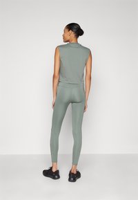 Top senza maniche di un verde oliva chiaro e leggings abbinati, realizzati in un tessuto liscio e elastico. L'outfit presenta un design aderente e accenti sottili.