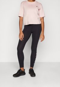 Rosa t-shirt med kortärm, rund halsringning, parat med svarta leggings som har en "ACTIVE"-tryck i gradientfärger. Svarta träningsskor.