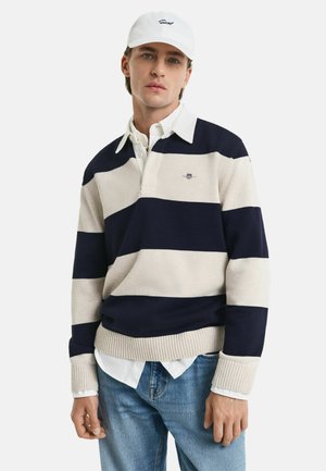 Gestreifter Strickpullover in Marineblau und hellbeige mit Kragen, ausgestattet mit gerippten Bündchen und Saum. Über einem weißen Hemd mit lässigen Jeans getragen.