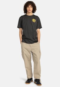 Sort bomulds T-shirt med et gult spiral grafik på brystet, parret med beige cargo bukser og sorte sneakers med en gummisål.