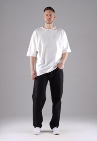 White oversized cotton t-shirt with short sleeves, paired with black denim pants and white sneakers. Simple design, no patterns or accents.