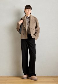 Tan double-breasted wool jacket, black wide-leg trousers, beige slip-on shoes, and a black bag. Zebra-striped top visible under the jacket.