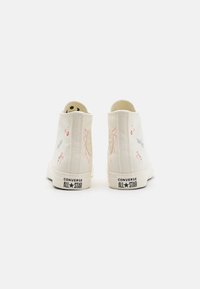 Zapatillas de lona de caña alta en color blanco roto con diseños florales bordados en rosa y gris. Con suela de goma y acentos de logo en negro.
