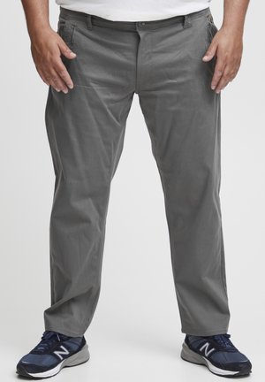 Grijze katoenen broek met een rechte snit, voorzien van voorzakken, riemlussen en een knoopsluiting. Gecombineerd met blauwe sportchoenen.