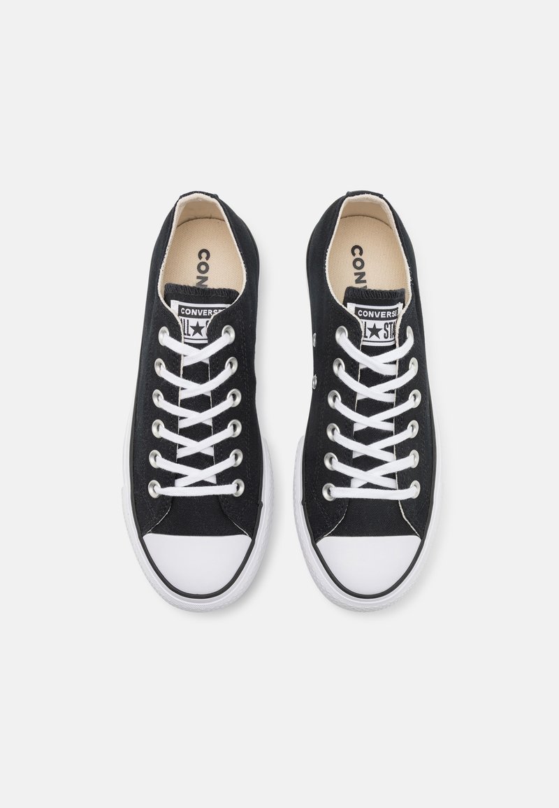 Coppia di sneakers Converse nere basse con punte in gomma bianca e lacci bianchi su uno sfondo chiaro uniforme.