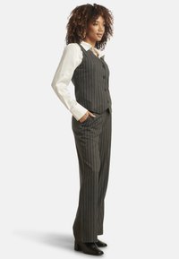 Striped gray suit with a tailored vest and wide-leg trousers, paired with a white collared shirt and black heeled boots.