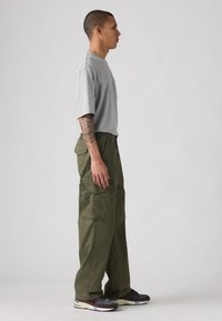 Gray short-sleeve t-shirt paired with olive green cargo pants featuring multiple pockets and a relaxed fit, complemented by brown and blue sneakers.