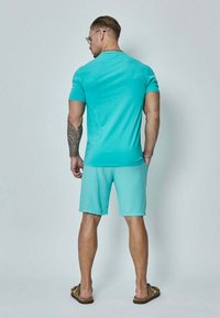 T-shirt en coton turquoise et short assorti, coupe décontractée. Présente un col rond et des coutures plates. Porté avec des sandales marron.