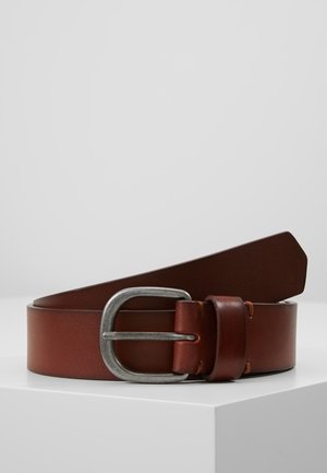 Ceinture en cuir marron avec une boucle en métal argenté, présentée enroulée sur une surface blanche avec un fond gris clair uni.