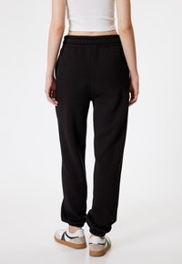 Zwarte joggers met een elastische tailleband en ingezette boorden, gemaakt van zachte stof, gecombineerd met witte sneakers met zwarte accenten.