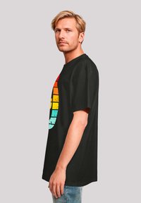 Schwarzes T-Shirt mit einem bunten Grafikdesign in Rot, Orange, Gelb und Türkis. Mit kurzen Ärmeln, lockerer Passform und aus weichem Baumwollmaterial.