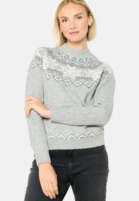 Sivi pleteni pulover z visokim ovratnikom, ki ima geometrijski vzorec v beli in modri barvi. Ima teksturirano površino in rebraste manšete.
