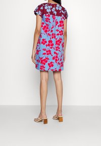 Květinové šaty s modrým tělem a vínovými rukávy, které mají květinové vzory v červené a modré barvě. Krátká délka a volný střih.