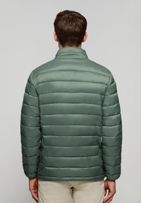 Chaqueta de plumas verde con un alto cuello, costuras horizontales y textura suave. Diseño ligero, adecuado para el clima frío.