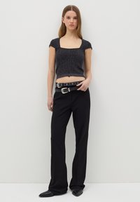Top corto de punto negro con escote cuadrado, combinado con pantalones negros de cintura alta y un cinturón negro con tachuelas. Zapatos planos de punta afilada.