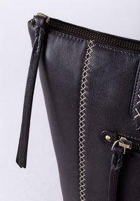 Dark brown leather bag featuring zipper closure, contrasting beige stitching, and a side pocket with brass hardware accents.