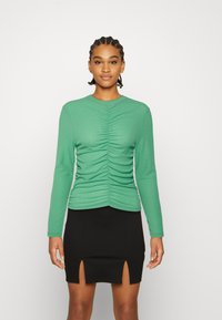 Top verde de manga longa com textura franzida na frente, combinado com uma saia preta com fendas frontais. Design ajustado e tecido canelado.