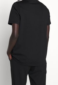 Musta puuvillainen t-paita, jossa on rento istuvuus, lyhyet hihat ja klassinen pyöreä pääntie. Paita on sileäpintainen ja yksivärinen ilman näkyviä kuvioita.