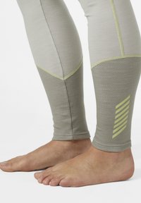 Leggings atléticos gris claro con paneles de malla, acentos verdes en contraste y un diseño a rayas en la parte inferior de la pierna, ajustados al tobillo.