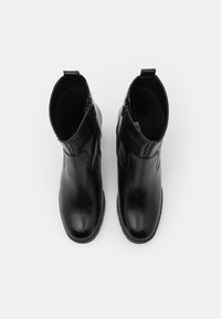 Botas de cuero negras hasta el tobillo con cremalleras laterales, puntera redondeada, textura suave y detalles de costura. Interior forrado para mayor comodidad.