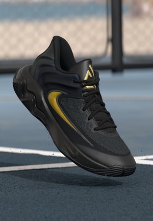 Black and gold athletic shoe suspended above a blue outdoor court with a white boundary line.