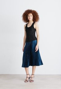 Top in paillettes nere su cui si adagia una gonna plissettata di lunghezza media in blu scuro. Tacchi neri con cinturini completano il look. Texture liscia e finitura lucida.