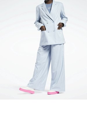 Osoba oblečená v světle modrém oversized dvouřadém saku a širokých kalhotách s bílými teniskami se zářivě růžovými podrážkami.