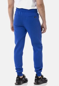 Königsblaue Jogginghose mit elastischem Bund, zwei Gesäßtaschen und schmal zulaufenden Beinen. Kombiniert mit schwarzen Sneakers mit einem eleganten Design.