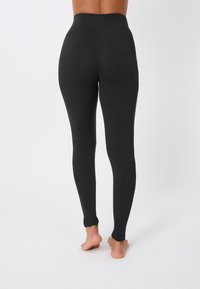 Legging noirs avec une taille haute. Fabriqués dans un tissu extensible et lisse. Longueur complète avec un design ajusté et sans coutures visibles.