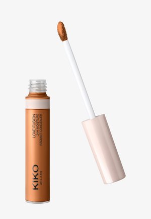 Tube de correcteur liquide étiqueté "Love Fusion 24H Correcteur Radiant Hydratant" avec applicateur en forme de patte de biche montrant une teinte beige moyen.