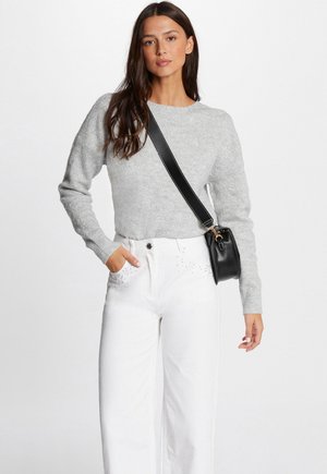 Pull en maille grise à manches longues, associé à un jean blanc taille haute avec des embellissements près des poches, et un petit sac noir en bandoulière.